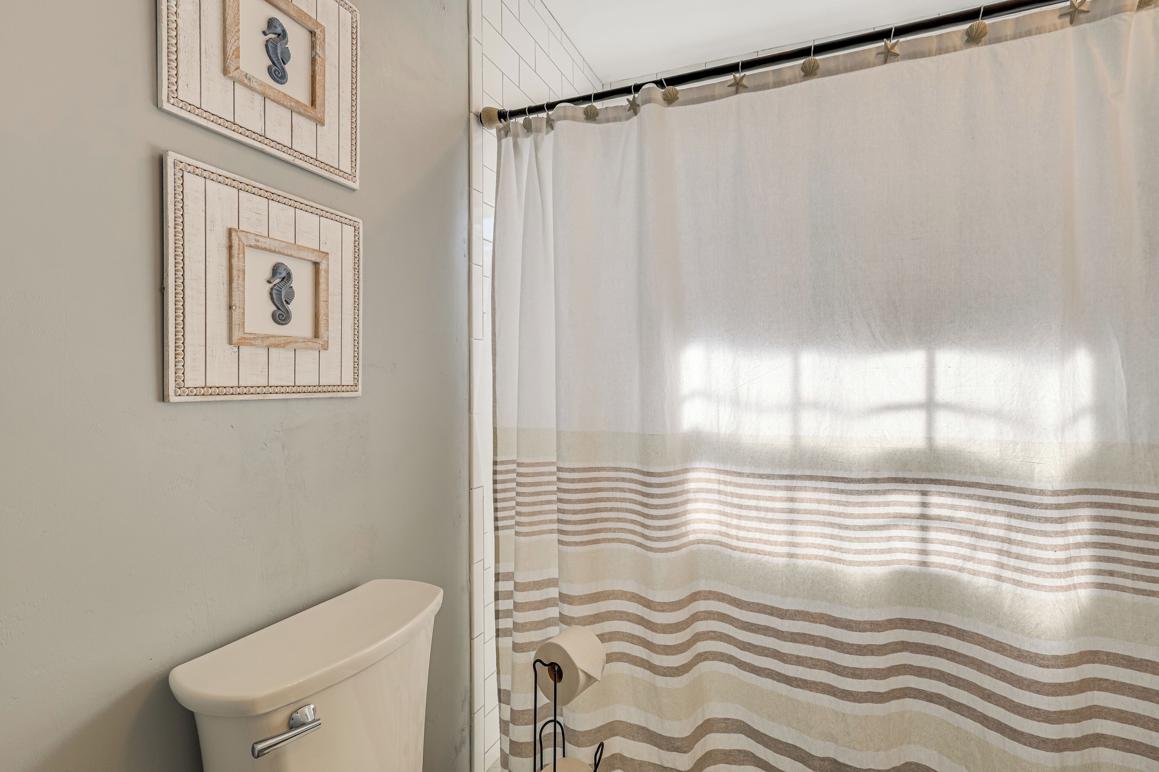 A bathroom with a toilet, a shower curtain with a striped pattern, and two framed pictures on the wall.