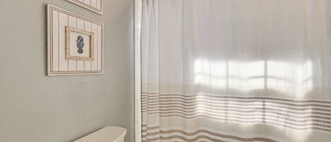 A bathroom with a toilet, a shower curtain with a striped pattern, and two framed pictures on the wall.