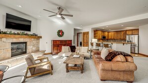 A spacious living room with a stone fireplace, a flat-screen TV, a ceiling fan, and a cozy seating area with a sofa and armchairs. - Ski-in/ski-out! Large Arrowhead Condo w/ Balcony (Edwards)