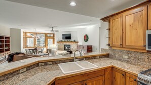 A kitchen with granite countertops, wooden cabinets, a double sink, a built-in oven, and a stone fireplace. - Ski-in/ski-out! Large Arrowhead Condo w/ Balcony (Edwards)