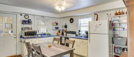 A kitchen with a dining table, chairs, a refrigerator, and various kitchen appliances.