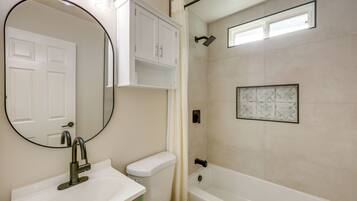 A bathroom with a white sink, a toilet, a bathtub, a showerhead, and a mirror.