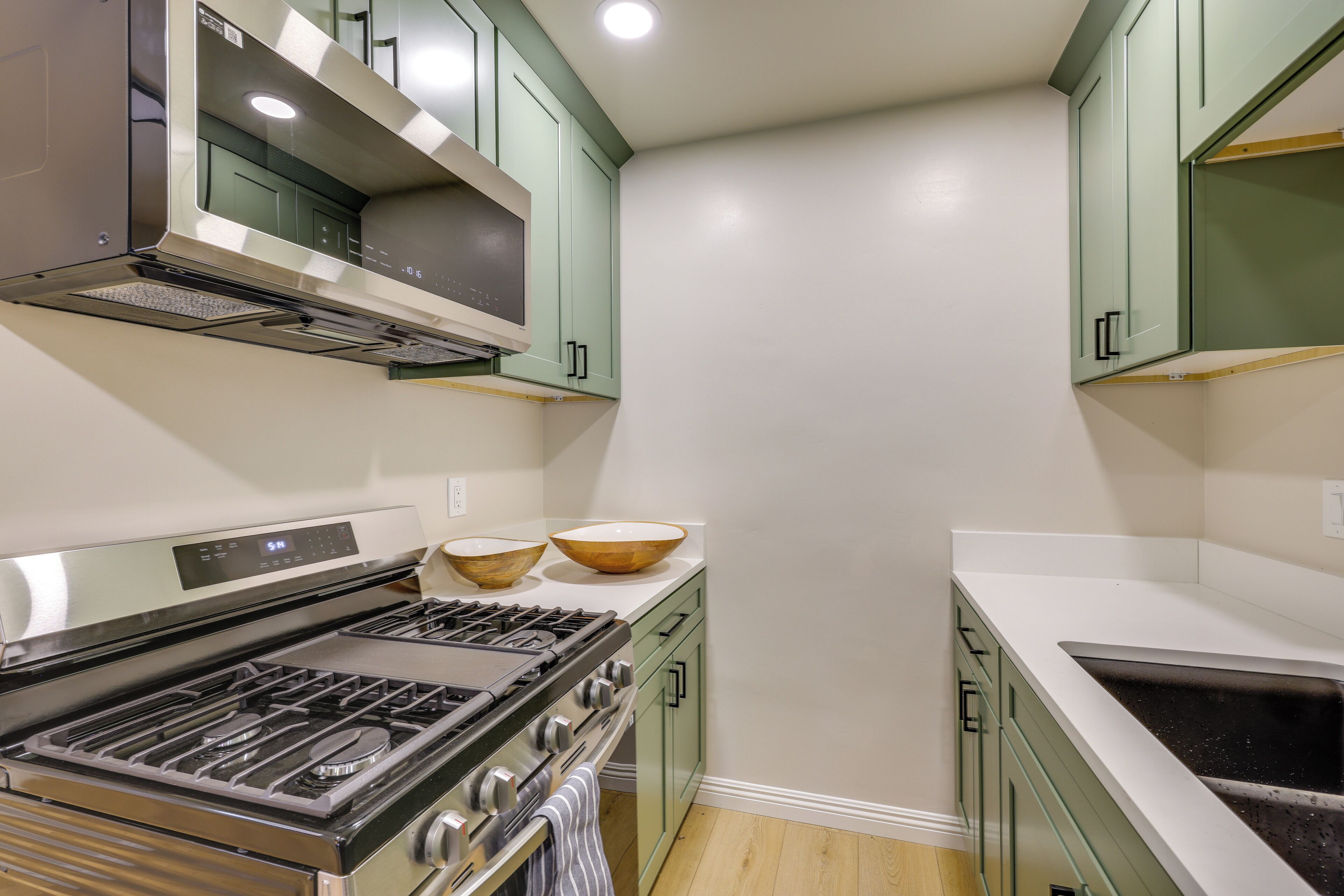 Una cocina con estufa de acero inoxidable, dos cuencos de madera en la encimera y armarios verdes.