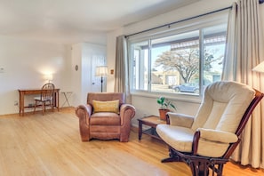 Una sala de estar con un sillón de cuero marrón, un sillón beige, una mesa de centro de madera y un comedor con mesa y sillas de madera.