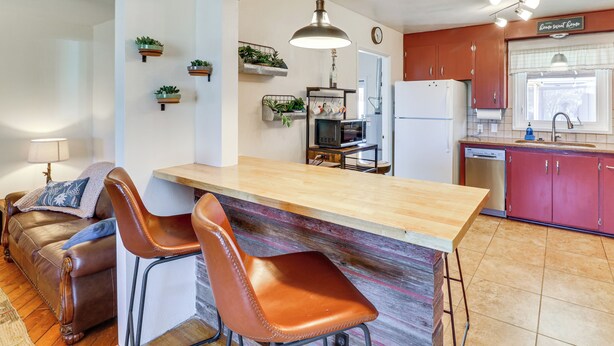Una cocina con una isla de madera, dos sillas de cuero marrón, techo de madera y un refrigerador.