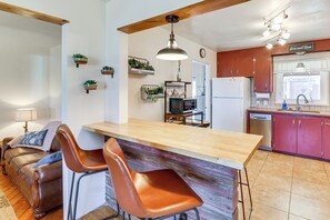 Una cocina con una isla de madera, dos sillas de cuero marrón, techo de madera y un refrigerador.