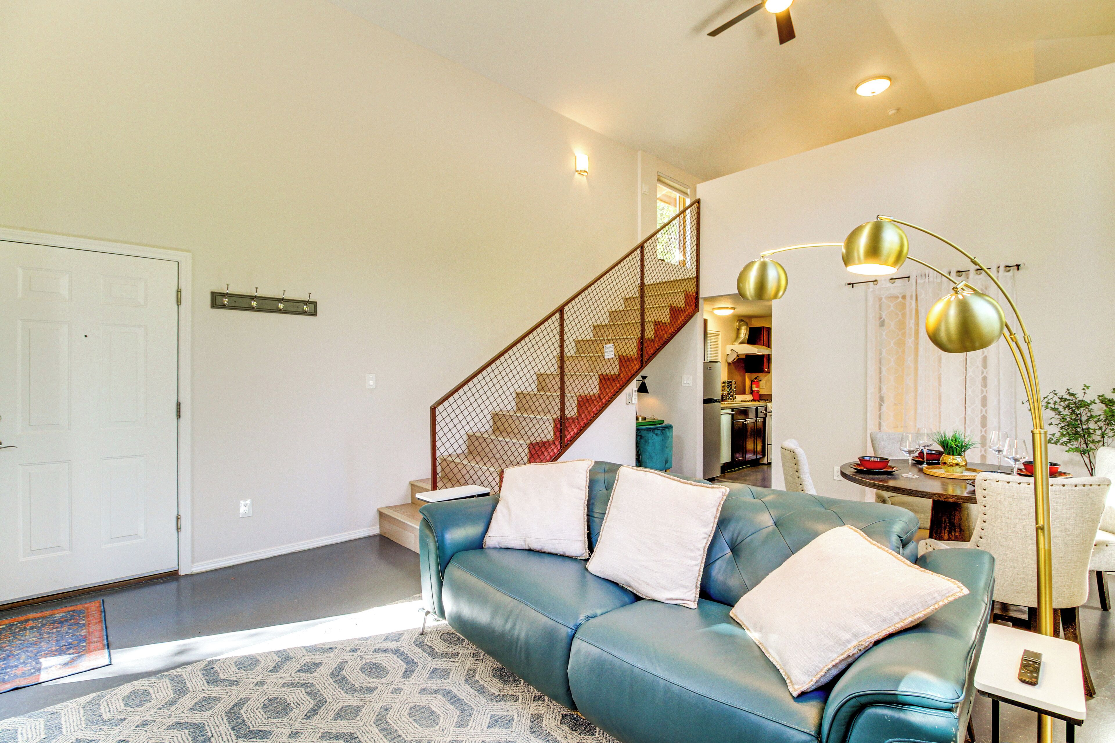 Ein modernes Wohnzimmer mit einem blauen Ledersofa, einer Treppe mit Holzgeländer und einem Essbereich mit Tisch und Stühlen.