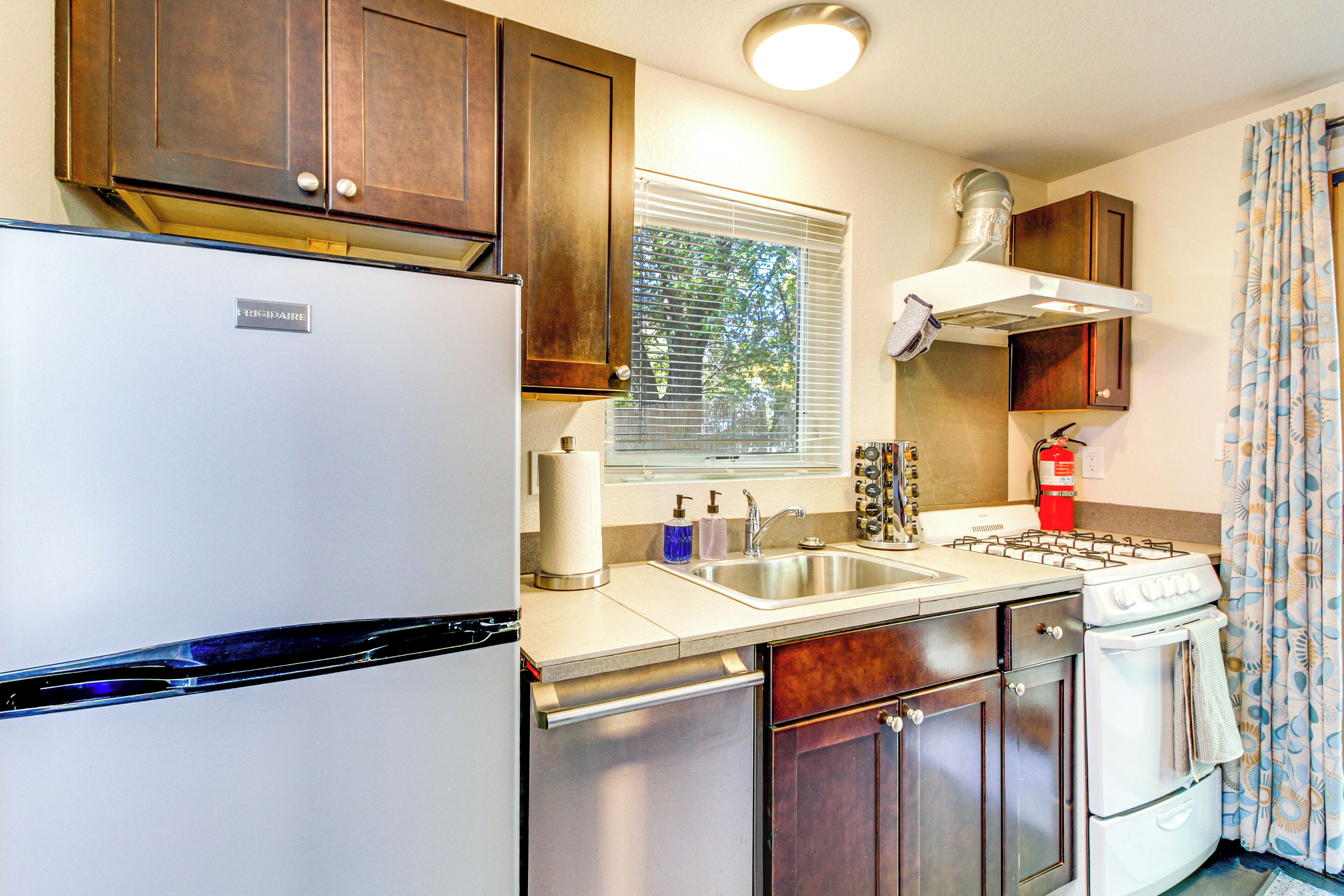 A compact kitchen with a refrigerator, stove, sink, and wooden cabinets.