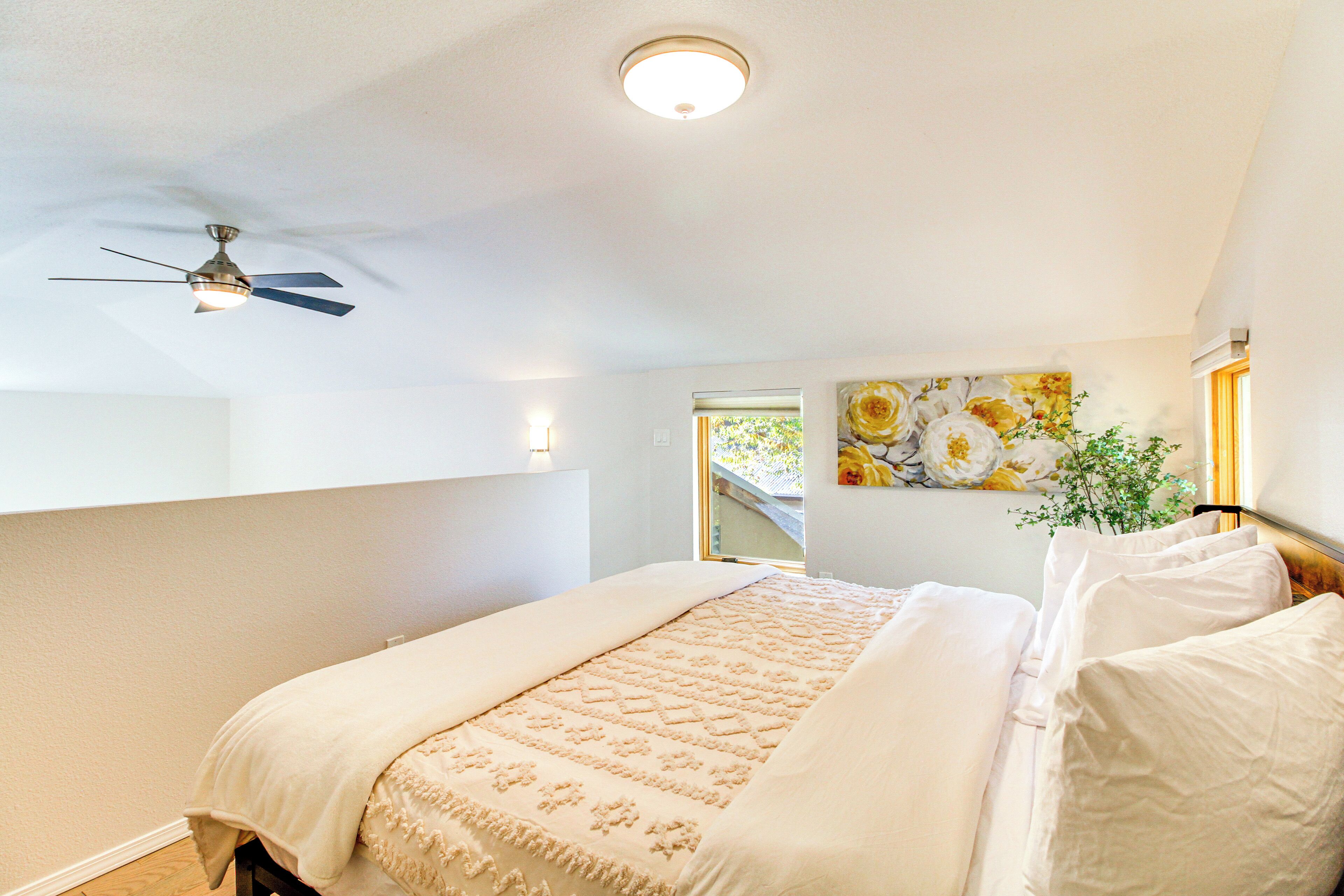 A bedroom with a bed, ceiling fan, and a window with a view of greenery.