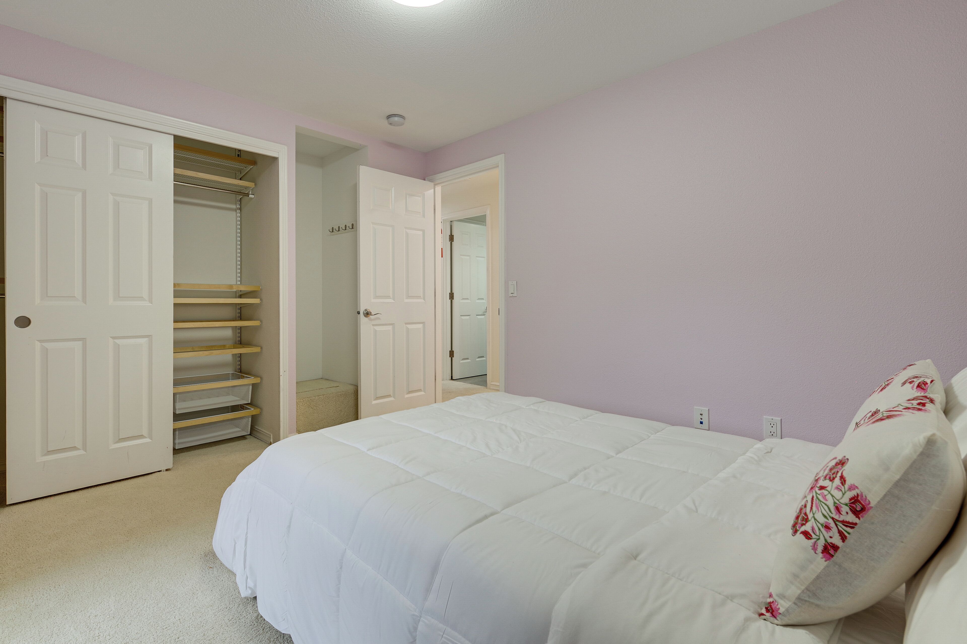 Un dormitorio con cama, un armario con las puertas abiertas y un pasillo que conduce a otra habitación.