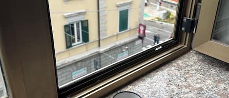 Janela com vista para um edifício com persianas verdes e um edifício de tijolos vermelhos ao fundo.