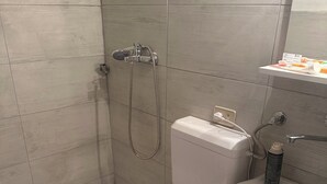 Kylpyhuone, jossa on suihku, wc, pesuallas ja pieni hylly, jossa on hygieniatuotteita.