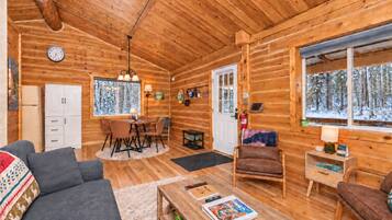 Interior acogedor de una cabaña de madera con comedor, sofá, sillón y chimenea.