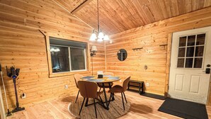 L’intérieur d’un chalet en bois comprend une table de salle à manger ronde, quatre chaises, un lustre, une grande fenêtre et une porte.