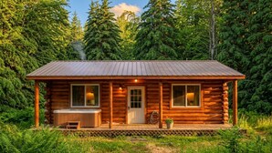 Une cabane en rondins avec un porche, un jacuzzi et une terrasse en bois.