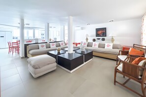 Un salon moderne avec un canapé d’angle, une table basse et un coin repas avec des chaises rouges.