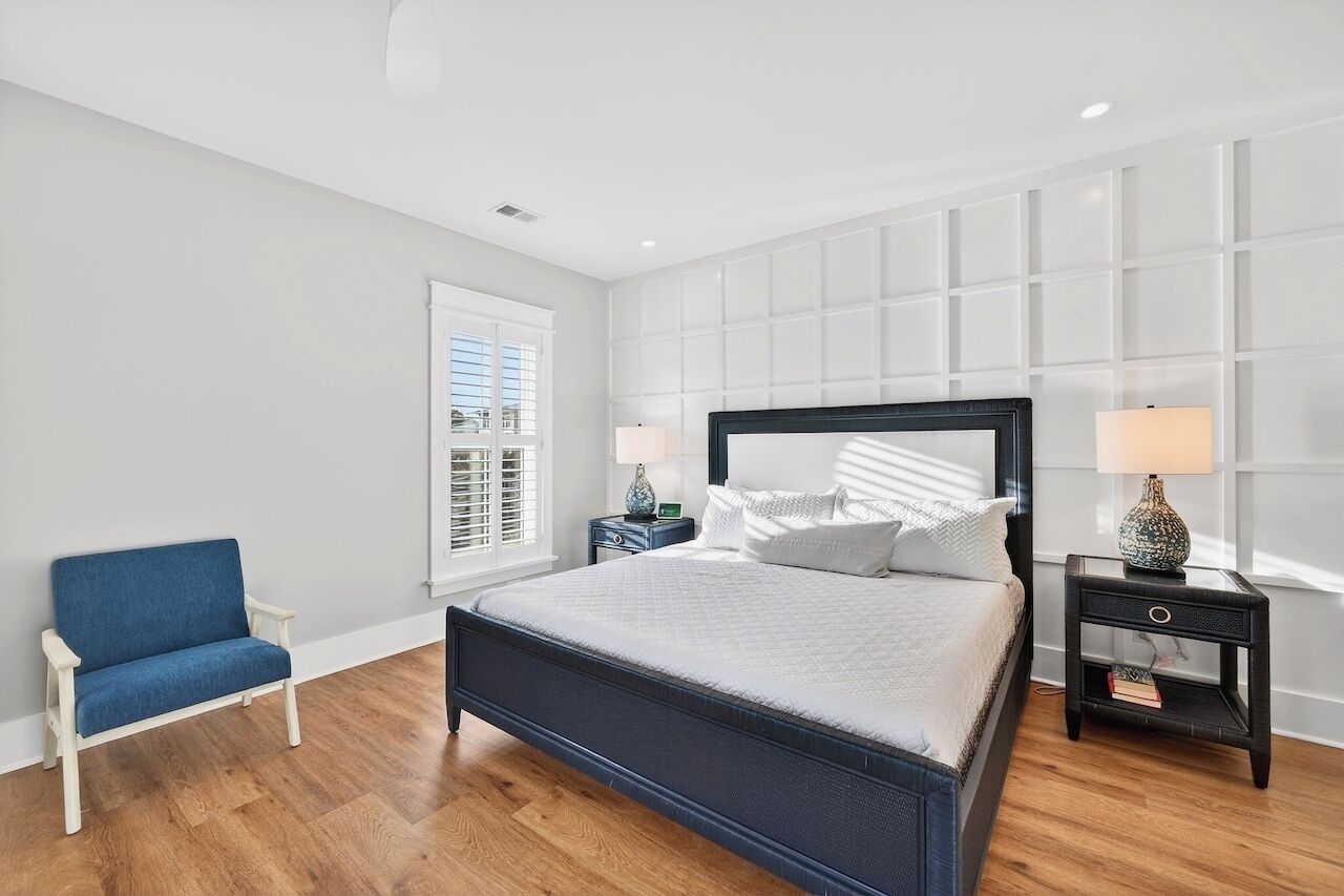 A bedroom with a bed, a chair, two nightstands, and a window with blinds.