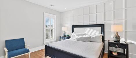 A bedroom with a bed, a chair, two nightstands, and a window with blinds.