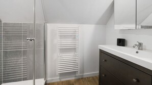 A modern bathroom with a glass shower enclosure, a white vanity with a dark cabinet, and a towel rack.