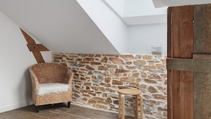 A room with a sloped ceiling, a stone wall, a wicker chair, a small wooden table, and a wooden door.