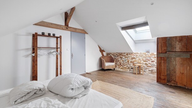 A bedroom with a lofted sleeping area, a wooden wardrobe, a stone wall, and a skylight.