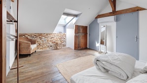 A loft bedroom with a sloped ceiling, wooden beams, a stone wall, a bed, a wardrobe, and a small seating area.