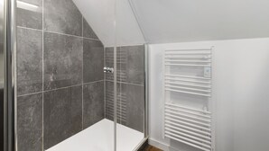 A shower with a glass door, a white radiator, and a tiled wall.
