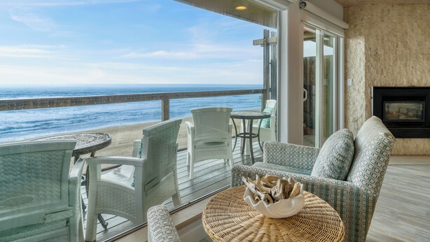 Een balkon met uitzicht op de oceaan, rieten meubels en een open haard.