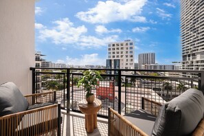 Ein Balkon mit Korbmöbeln, einer Topfpflanze und Blick auf eine Stadtlandschaft mit Gebäuden.