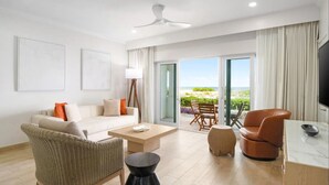 Un salon moderne avec un canapé blanc, un fauteuil en osier, une table basse et un téléviseur posé sur un meuble.