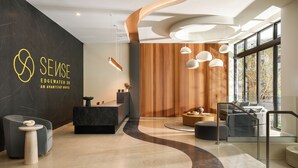 A modern hotel lobby with a reception desk, seating area, and large windows.