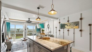 Une cuisine moderne dotée d’un grand îlot central, de luminaires suspendus et offrant une vue sur l’extérieur.