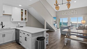 Een moderne keuken met witte kasten, een groot eiland en uitzicht op het strand door de ramen.