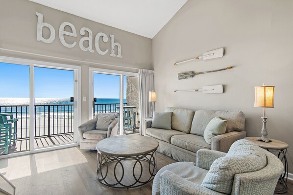 Ein Wohnzimmer mit Blick auf den Strand, ausgestattet mit einer Couch, Sesseln, einem runden Couchtisch und Wanddekoration.