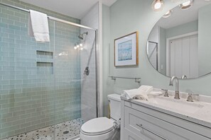 Ein Badezimmer mit Duschkabine aus Glas, Toilette, Waschbecken mit Spiegel und einem gerahmten Bild an der Wand.