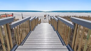 Een houten looppad dat naar een strand leidt, met een helder uitzicht op de oceaan.