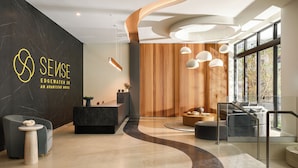 A modern hotel lobby with a reception desk, seating area, and large windows. - Brand New Luxury Hotel + Rooftop Pool + Gym + Near Design District | Sense28 (Miami)