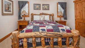Un dormitorio con un cabecero de madera rústica, colcha con estampados de animales, dos lámparas de noche y cuadros en las paredes.