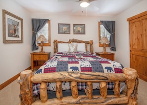 Ein Schlafzimmer mit einem rustikalen Holzbettgestell, einer Decke mit Tiermotiven, zwei Nachttischlampen und gerahmten Bildern an den Wänden.