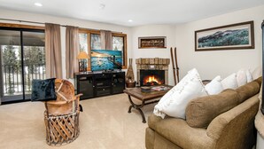 Una sala de estar con chimenea, televisor, sofá y vista al exterior.