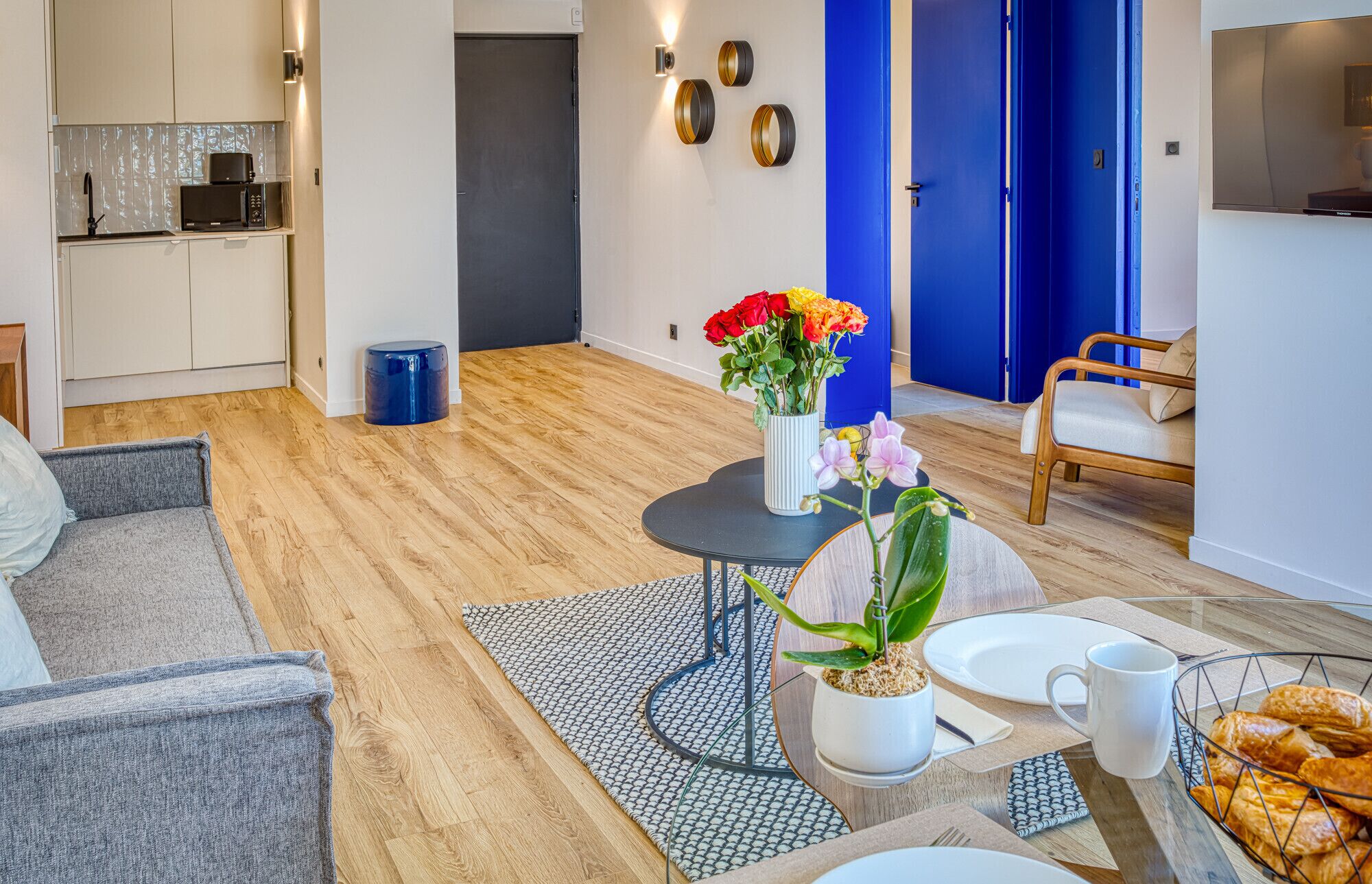 A modern living room with a dining area, a kitchen in the background, and a blue door.