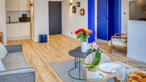 Ein modernes Wohnzimmer mit Essbereich, einer dahinterliegenden Küche und einer blauen Tür.
