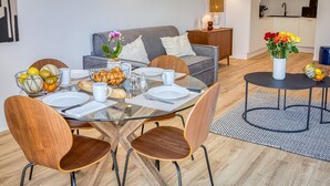 Ein moderner Essbereich mit einem Glastisch, Holzstühlen und einem grauen Sofa im Hintergrund.