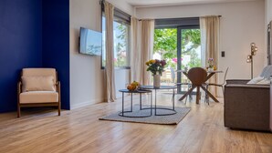Ein modernes Wohnzimmer mit einem beigen Sessel, einem runden Couchtisch und einem Essbereich mit Tisch und Stühlen.