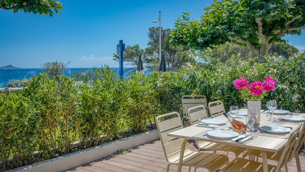 Ein Essbereich im Freien mit Blick auf das Meer, eine Holzterrasse und ein Tisch für zwei Personen mit Stühlen.