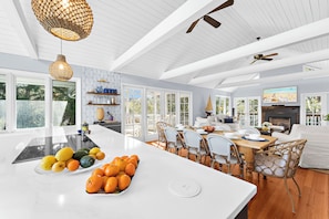 Cocina amplia con una isla grande, mesa de comedor de madera y sillas. Hay ventanas grandes y un ventilador de techo.