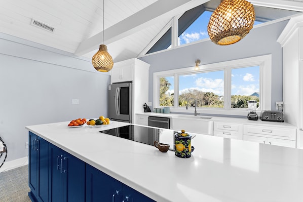 A modern kitchen with a large island, white countertops, blue cabinets, and a view of the outdoors through a large window. - Easy beach access and coveted Seabrook amenities (Seabrook Island)