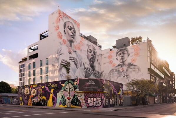 Un edificio con un gran mural en su fachada, que presenta diversos elementos artísticos y un anuncio destacado.