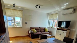 A modern living room with a wooden dining table, a sofa, and a TV. - Apartment Jelena, modern new, 200m to the beach, free of charge. W-LAN and parking (Vir)
