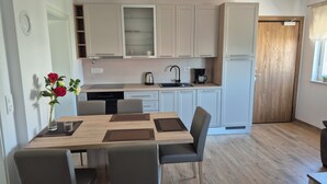 A modern kitchen with white cabinets, a wooden dining table, and a vase with flowers. - Apartment Jelena, modern new, 200m to the beach, free of charge. W-LAN and parking (Vir)